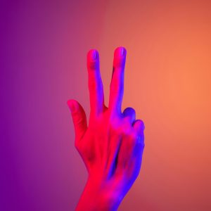 A hand making a peace gesture in vibrant neon lighting, ideal for creative and abstract stock imagery.